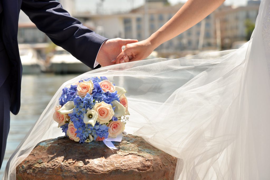 Le mani degli sposi e il bouquet davanti al mare